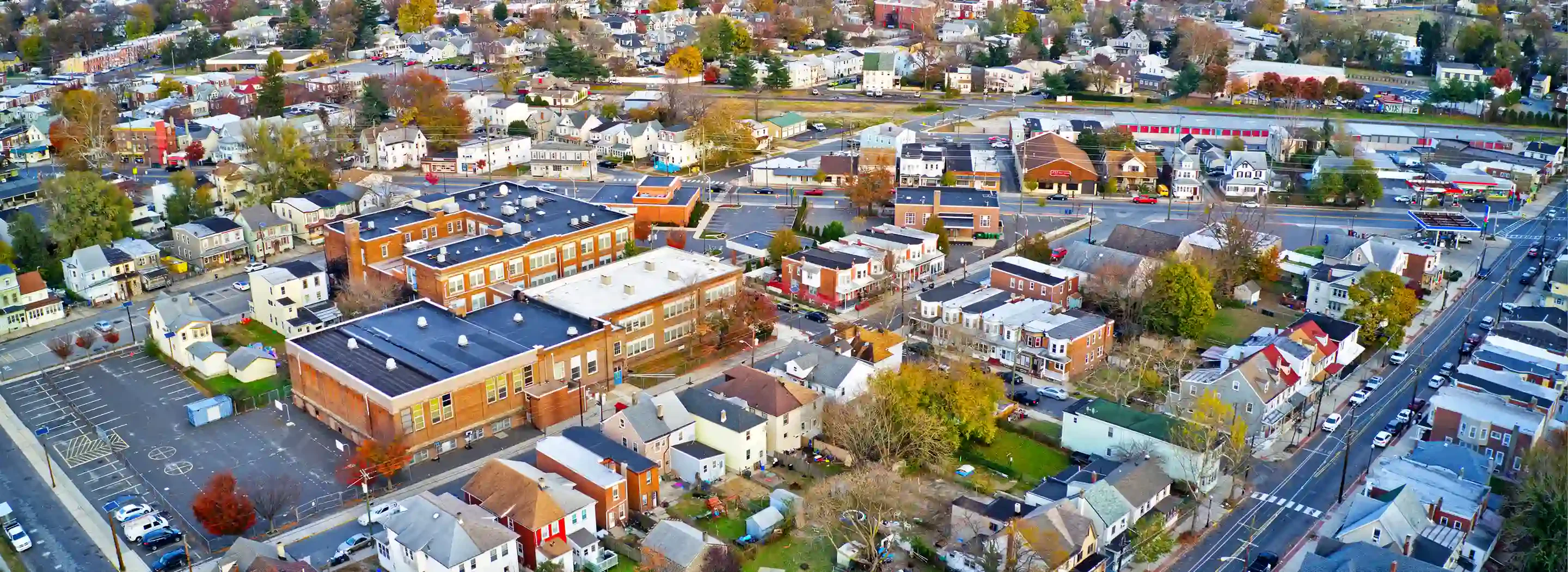 Aerial view of a small town showcasing residential areas, schools, and streets lined with colorful houses and trees in autumn foliage.